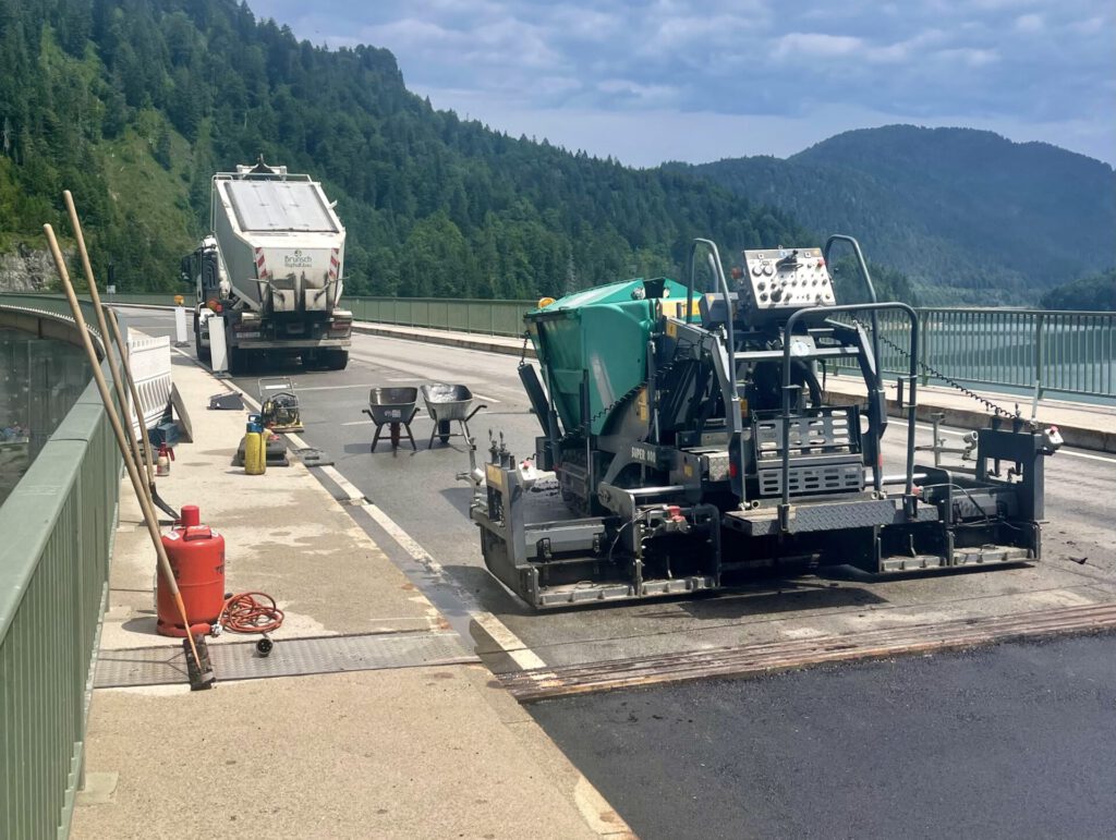 Fachmännische Teerarbeiten an einer Brücke durch das Team der Florian Brunsch GmbH aus Straßlach. Arbeiter bringen frischen, heißen Asphalt auf der Brückenoberfläche auf, um die Fahrbahn zu erneuern.