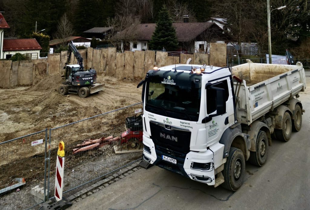 Professioneller Aushub einer Baugrube durch die Florian Brunsch GmbH in Straßlach. Ein moderner Bagger steht am Rande des präzise ausgehobenen Grundstücks, bereit für die nächsten Schritte des Tiefbaus.
